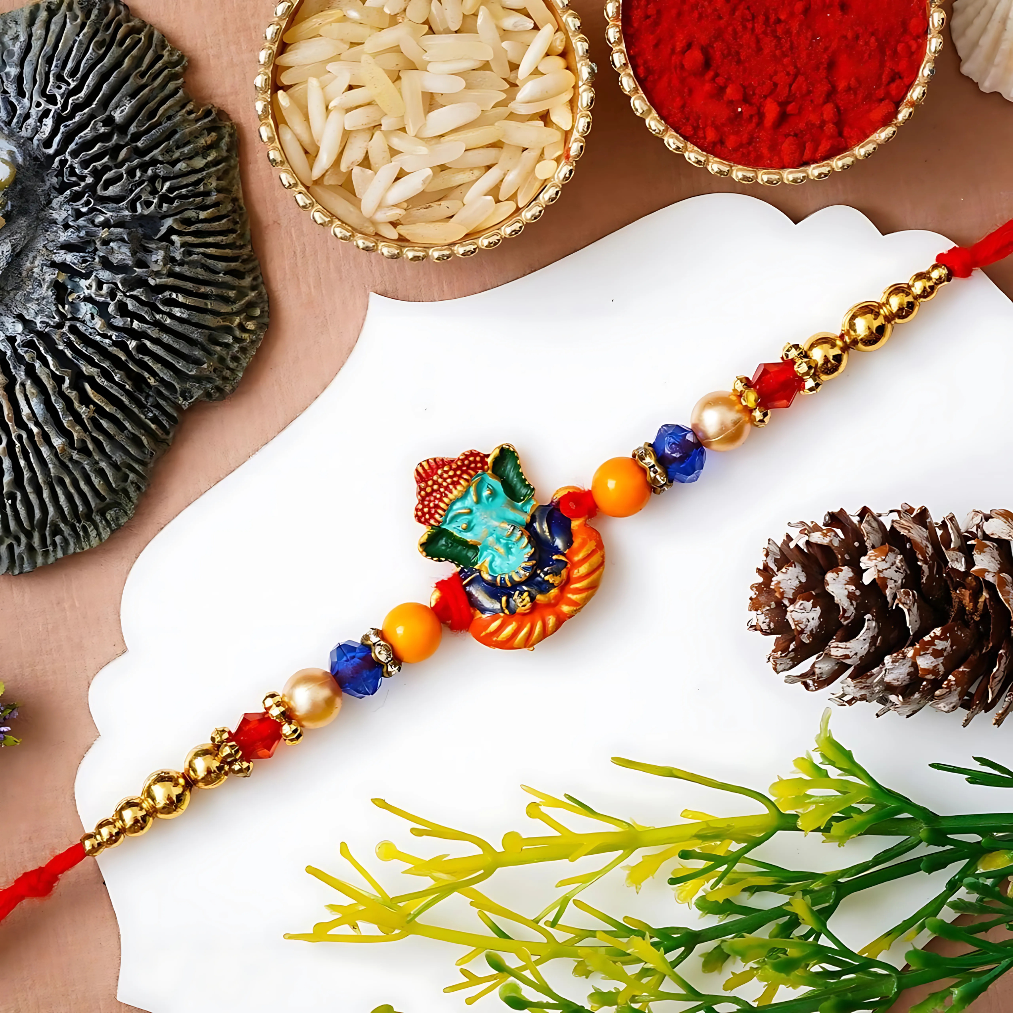 Ganesha Rakhi with colorful enamel Ganpati charm, red thread, and multi-color beads on festive background