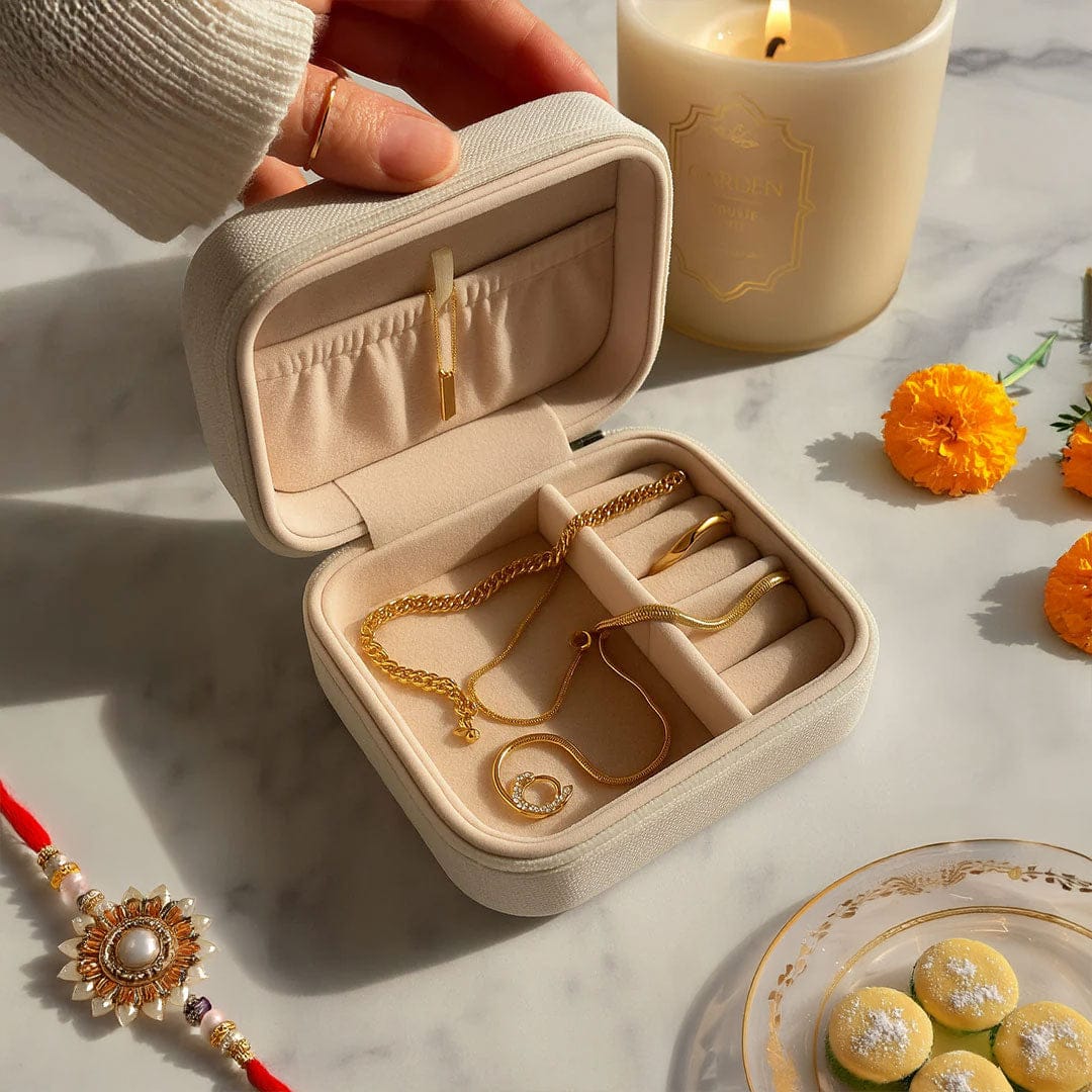 Hand holding an open travel jewellery box with gold chains inside, candlelit Rakhi setup in background